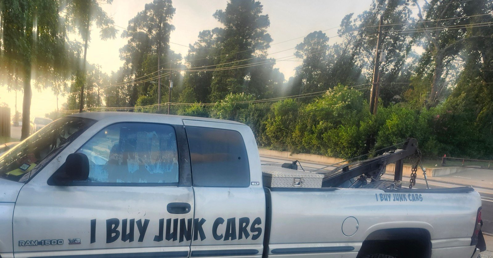 A pickup with a tow boom, lettered &lsquo;I Buy Junk Cars&rsquo; along the door and bedside.